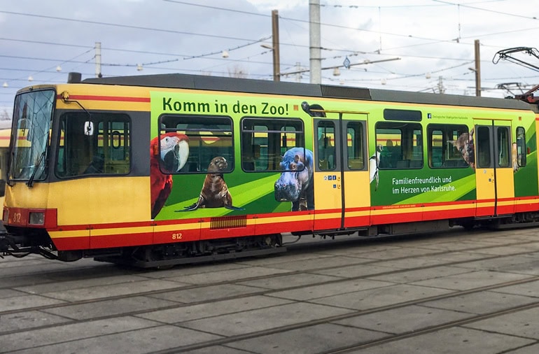 Eine gelb-rote Straßenbahn mit Tierbildern und einem Text, der für einen Zoo wirbt, parkt auf den Straßenbahnschienen.