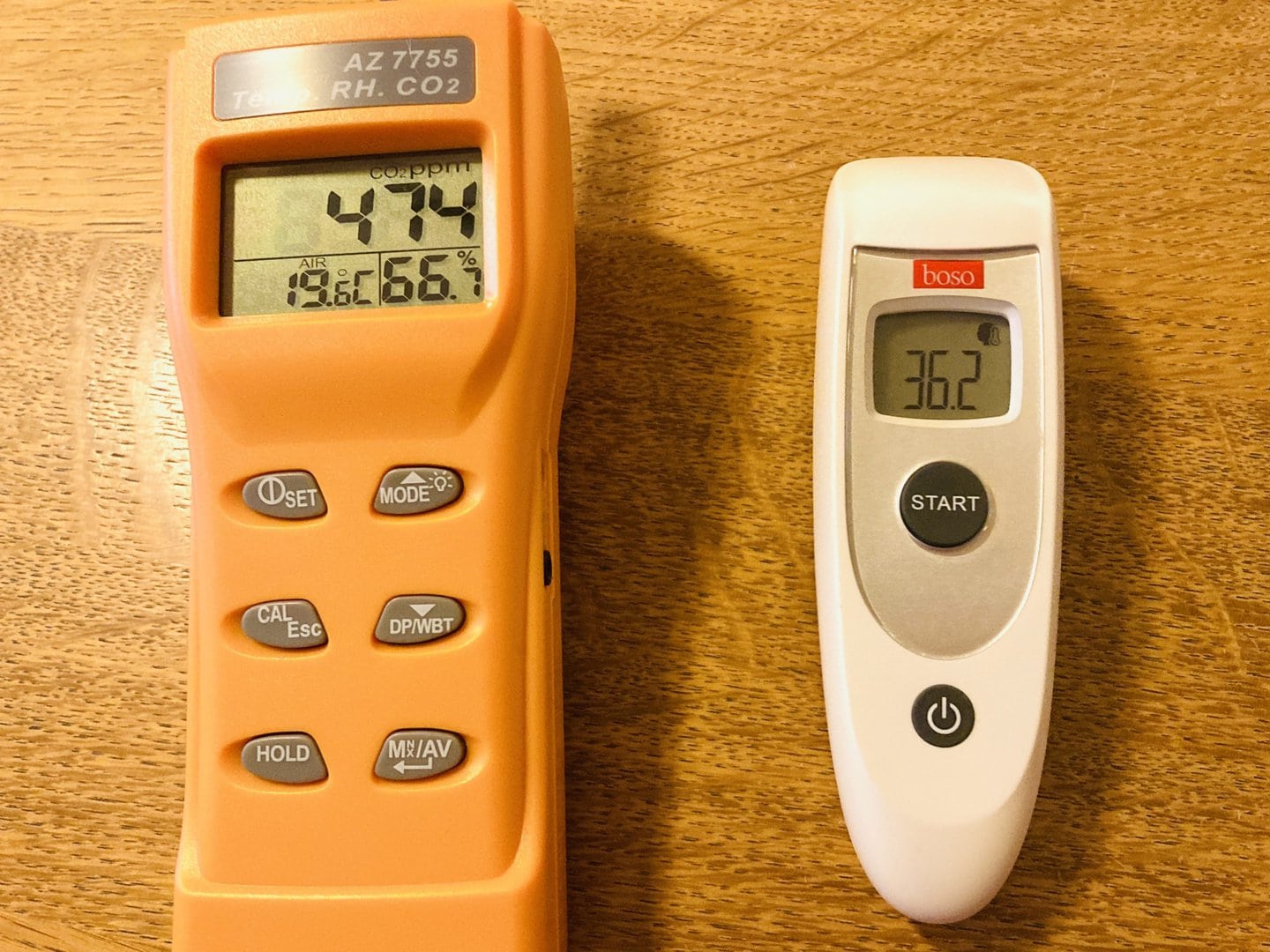 Ein orangefarbenes digitales CO2-Messgerät und ein weißes digitales Thermometer auf einer Holzoberfläche.