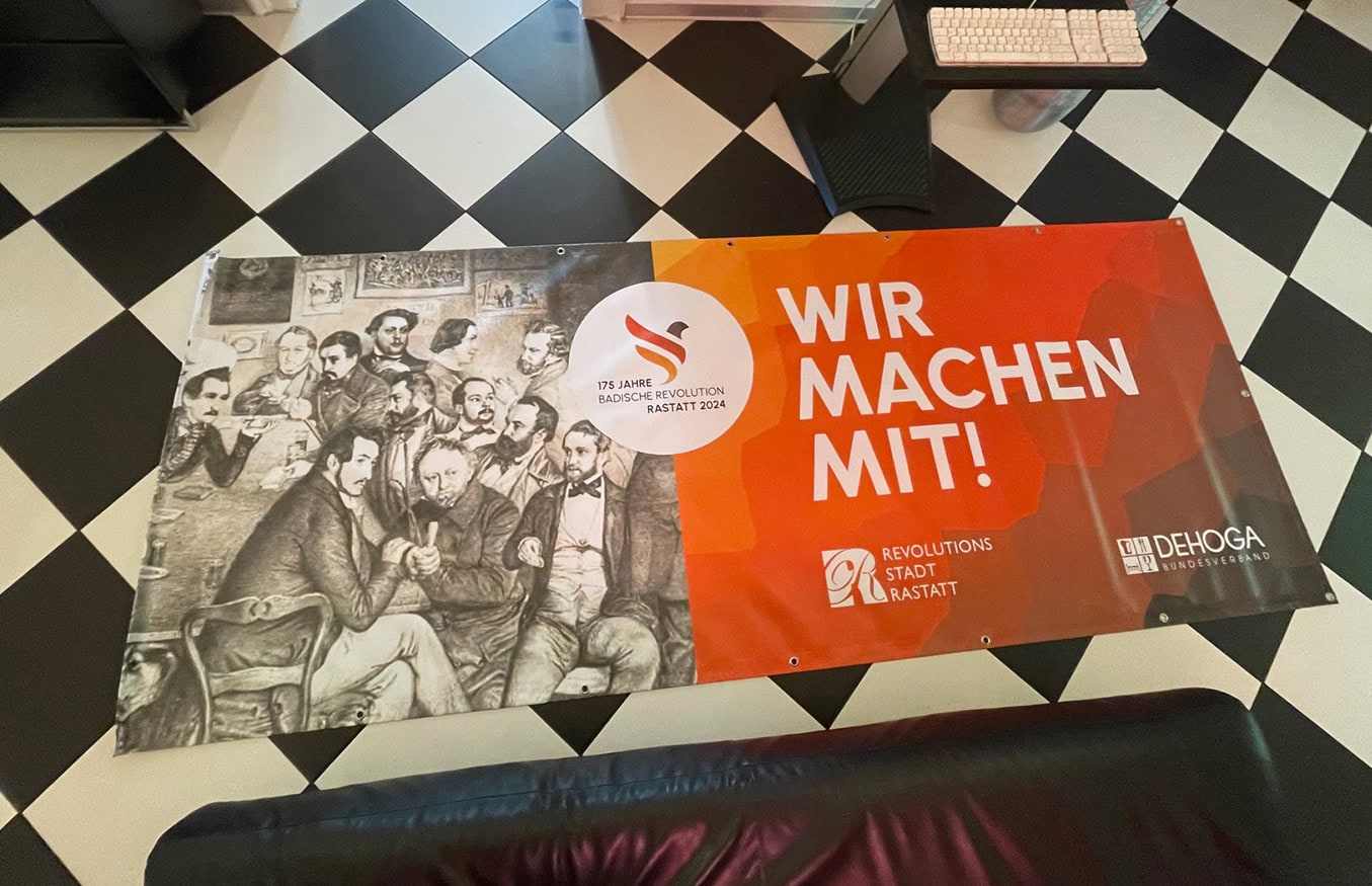 Banner auf dem Boden mit einem historischen Bild links und dem deutschen Text „WIR MACHEN MIT!“ rechts.