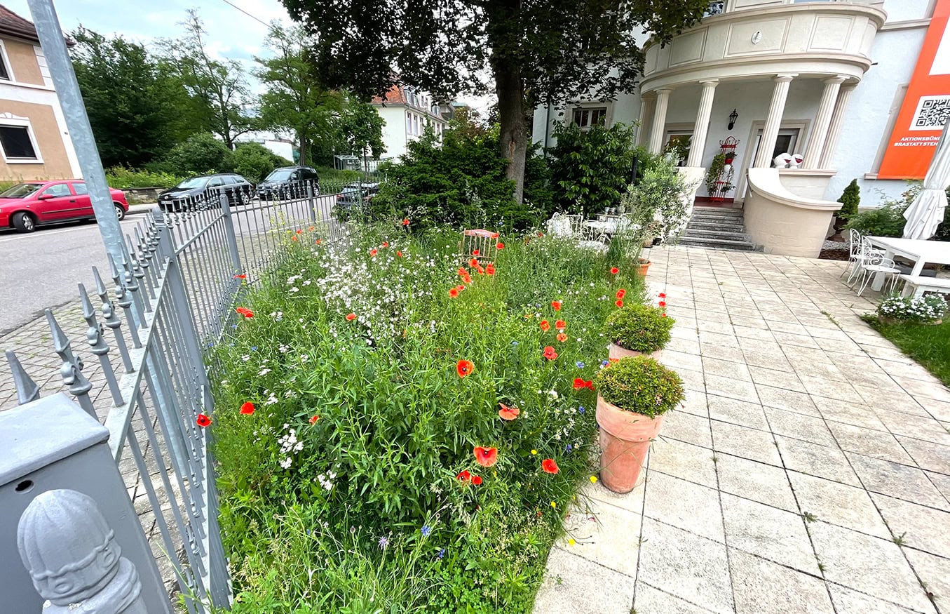 Ein Garten mit roten und weißen Blumen neben einem gefliesten Gehweg, der zu einem weißen Gebäude mit Säulen führt.