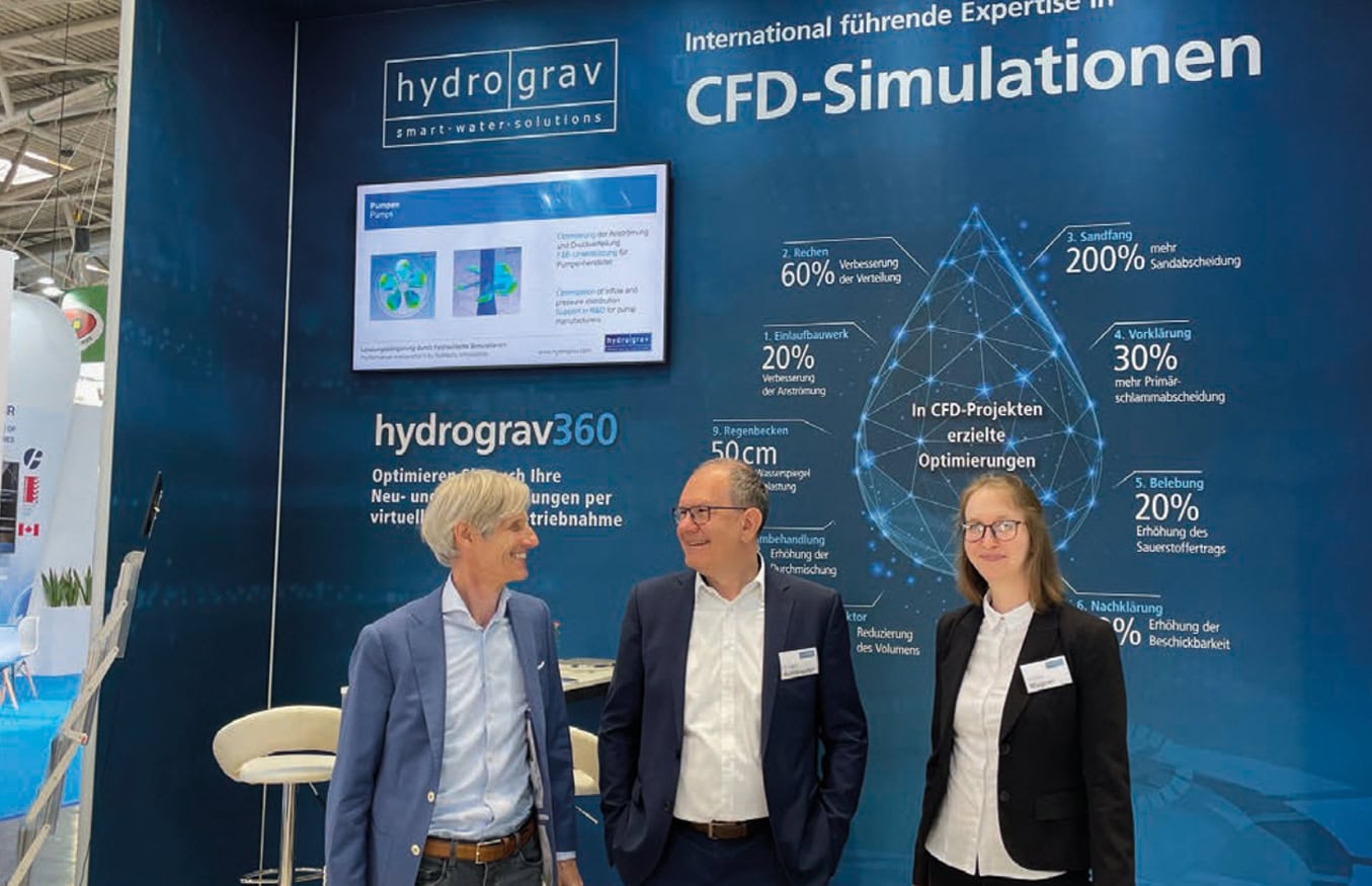 Drei Personen in Businesskleidung stehen vor einem blauen Messestand für CFD-Simulationen von hydrograv.