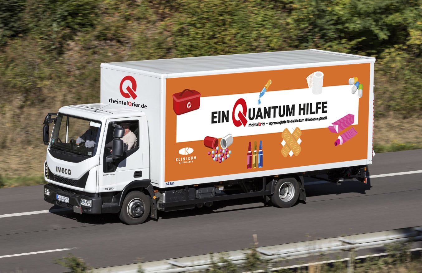 Ein Iveco-Lieferwagen mit der bunten Grafik „Eine Quantenhilfe“ fährt auf einer Autobahn mit viel Grün im Hintergrund.